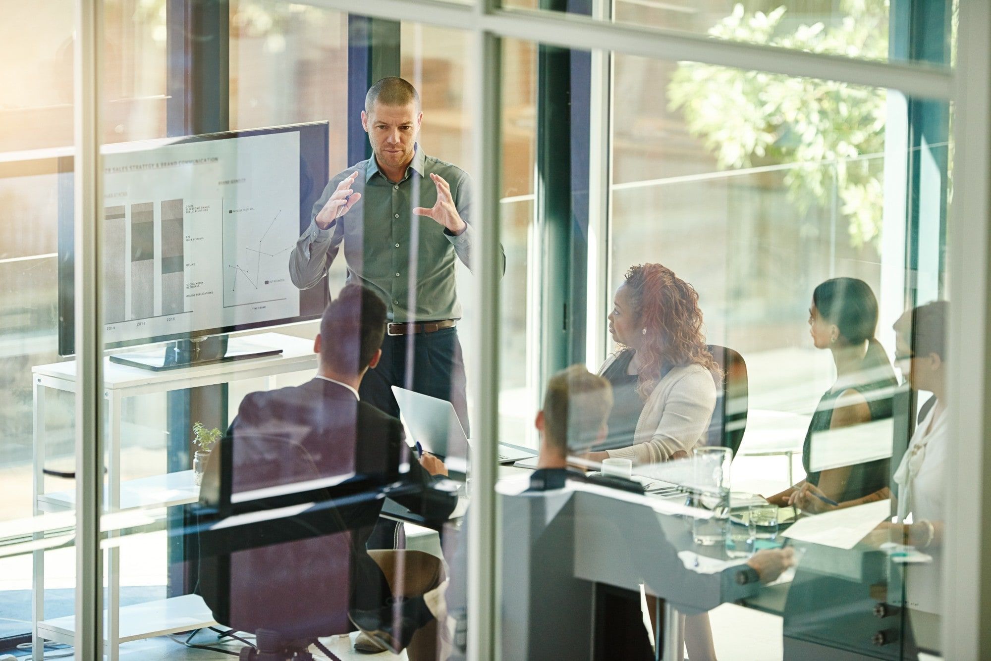 A team reviewing charts on a screen in a glass-walled meeting room.